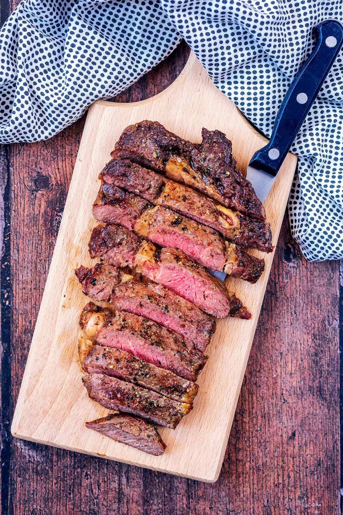 Sliced cooked steak on a wooden board with a knife.