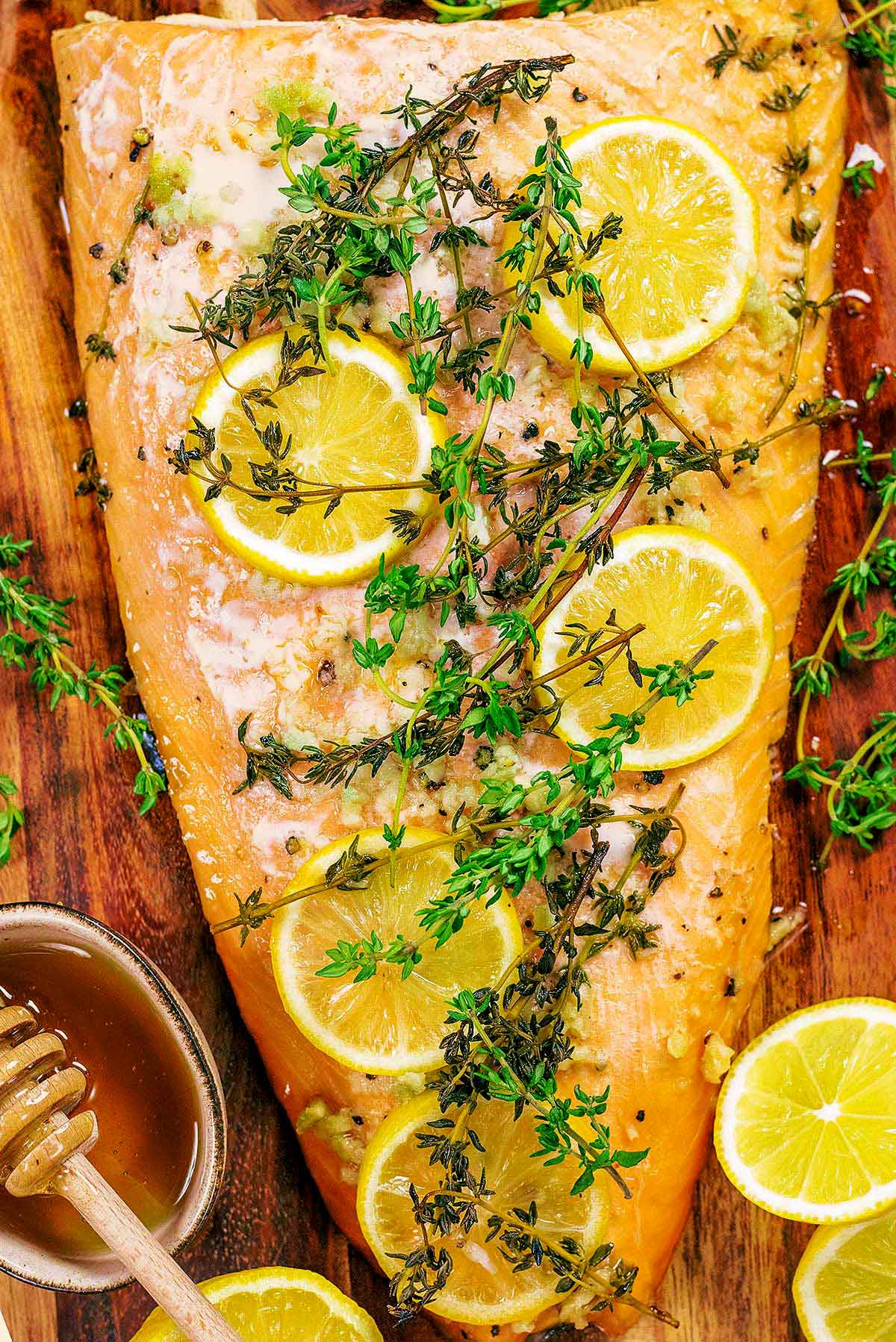 Cooked side of salmon with lemon slices and sprigs of thyme on it.