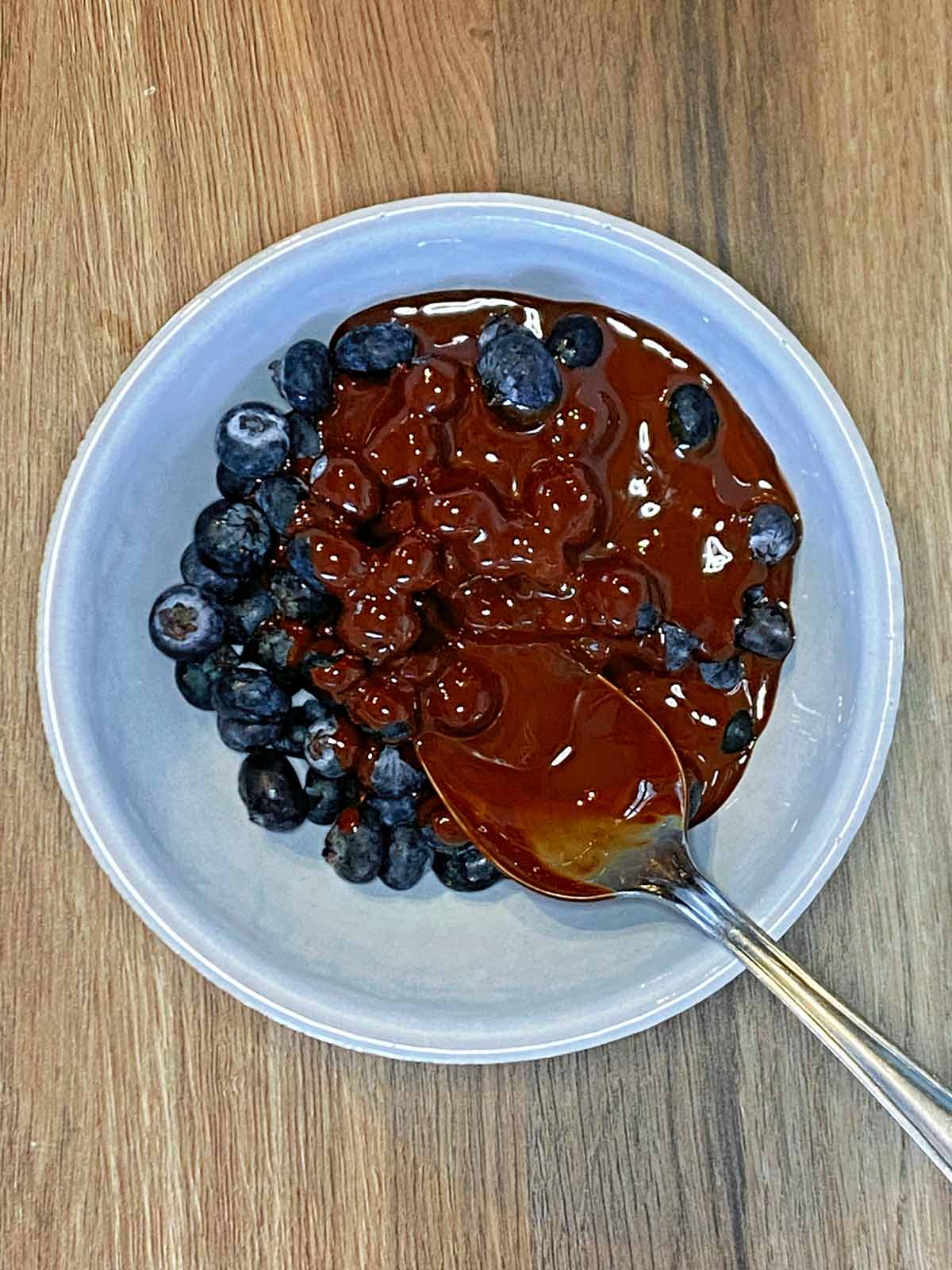 Blueberries in a bowl with melted chocolate being spooned over them.