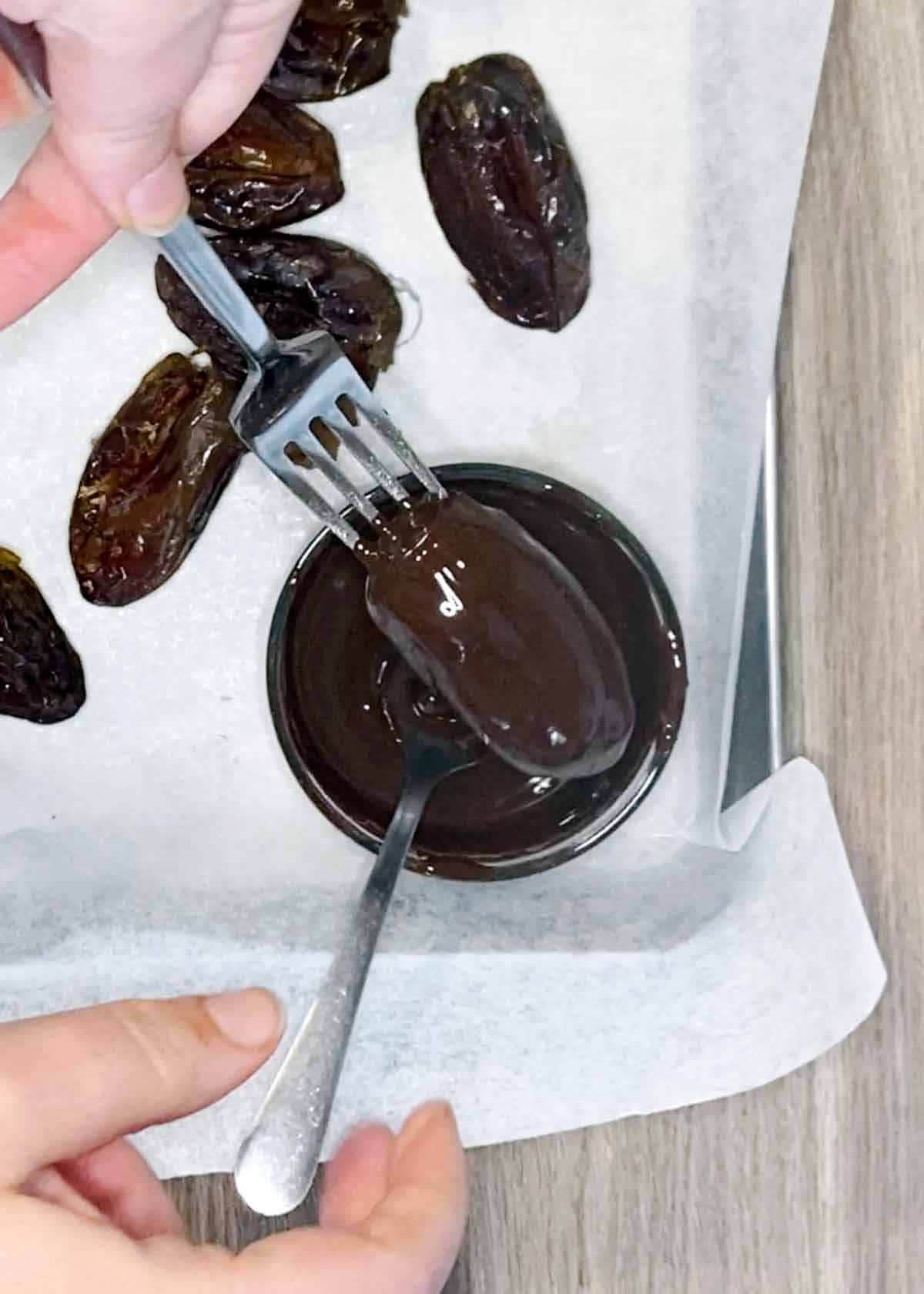 A date on a fork being dipped into melted chocolate.