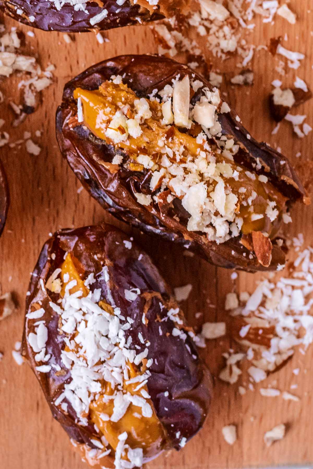 Two medjool dates stuffed with peanut butter with crushed nuts and desiccated coconut on them.