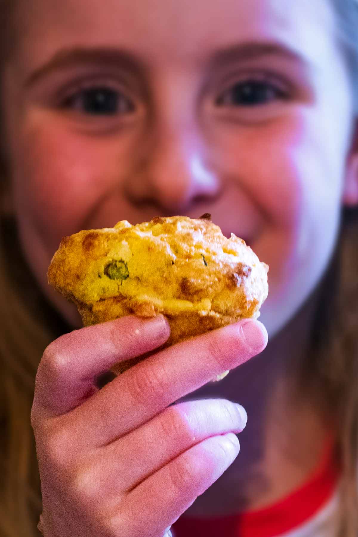 A female child holding a muffin in front of her face.