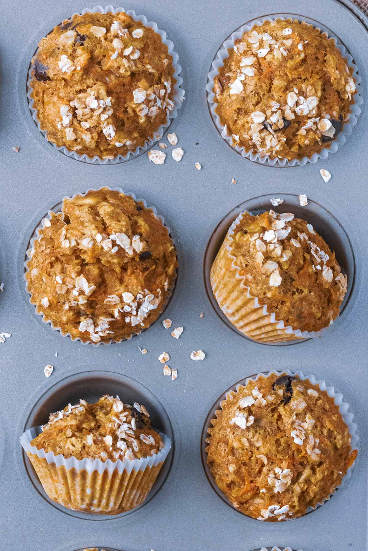 Six banana muffins in a baking tray, two muffins are turned on their sides.