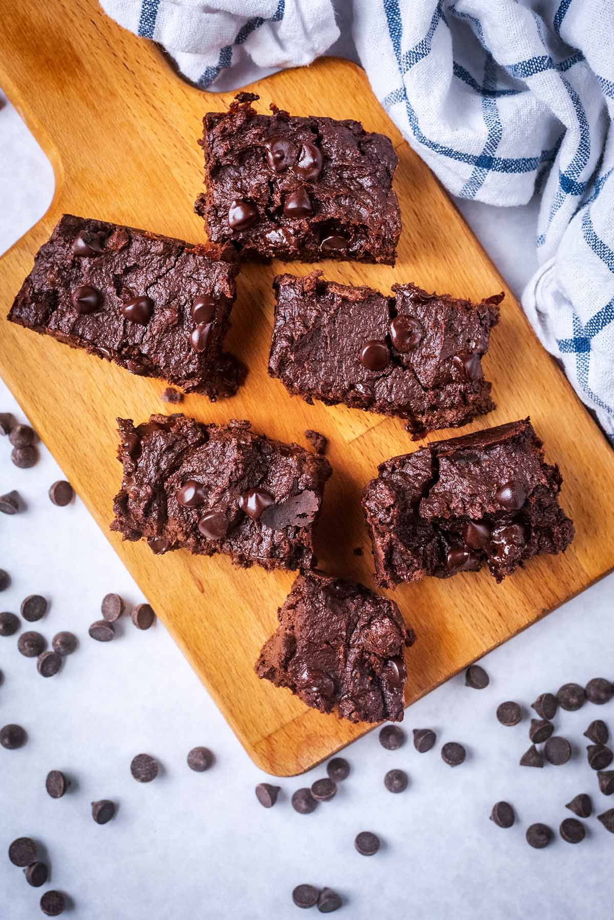 Six chocolate Brownies on a wooden serving board surrounded by chocolate chips.