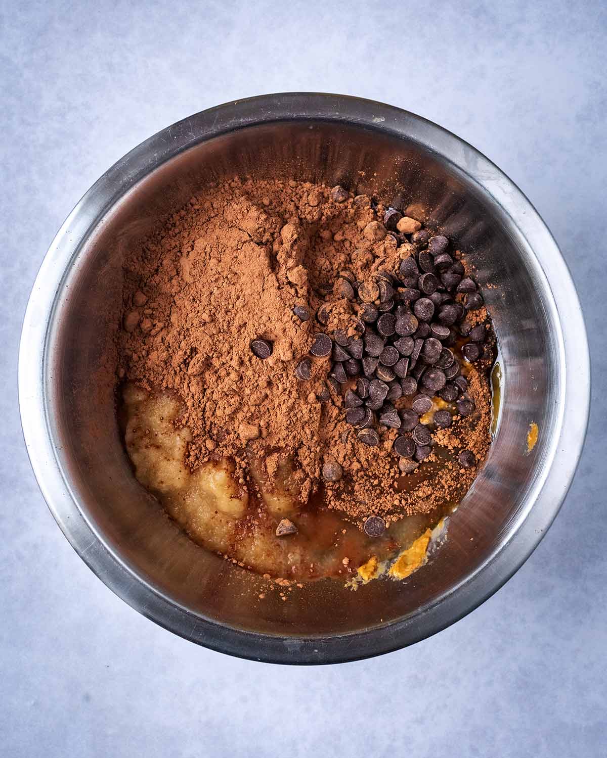 A mixing bowl containing applesauce, cocoa, nut butter, maple syrup and chocolate chips.