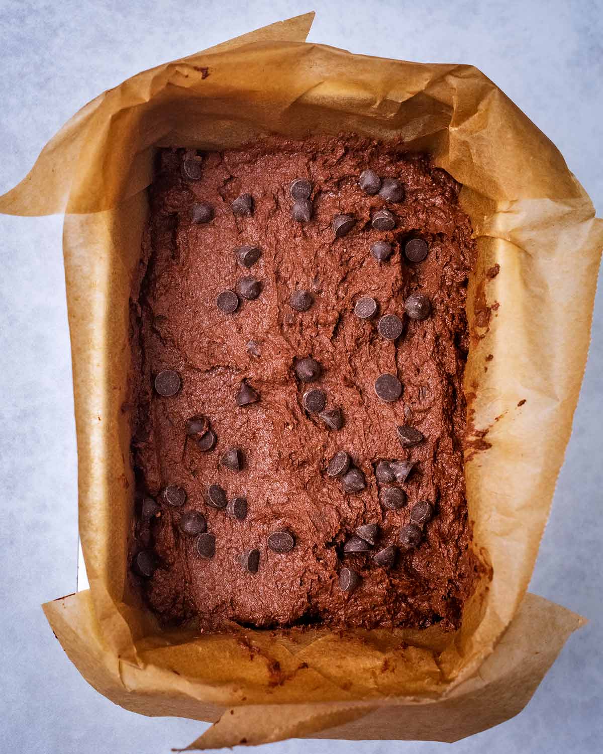 Brownie batter in a lined baking tin with chocolate chips scattered over the top.