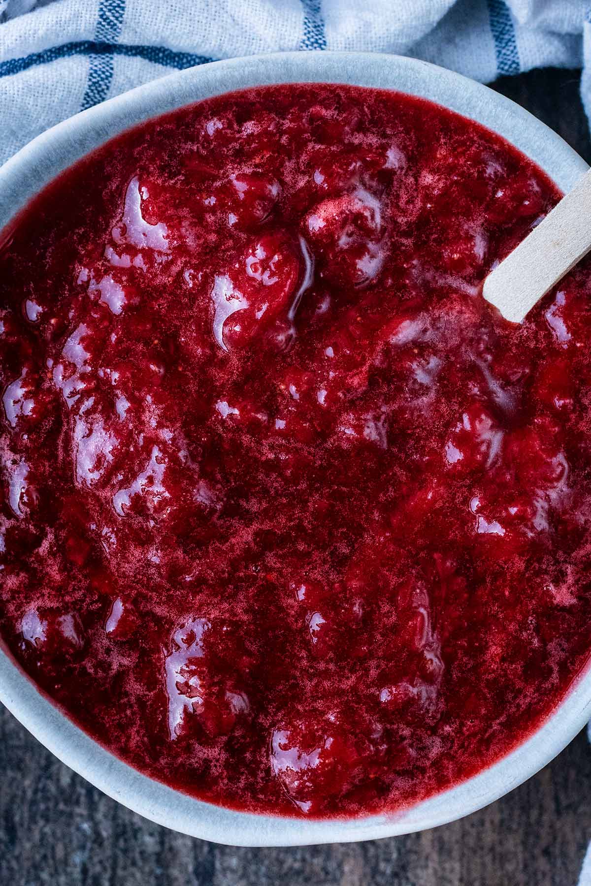 a bowl of strawberry compote next to a checked towel.