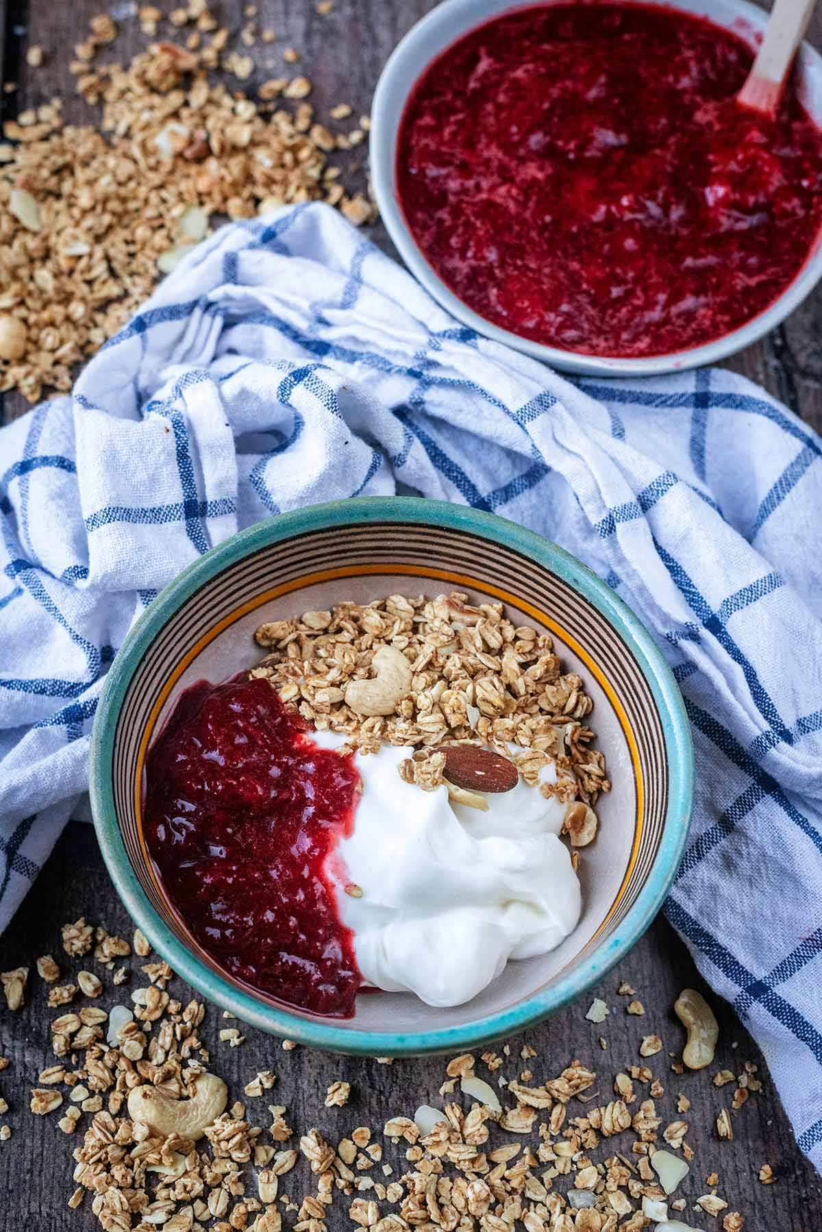 A bowl of yogurt, granola and compote next to a bowl of more compote.