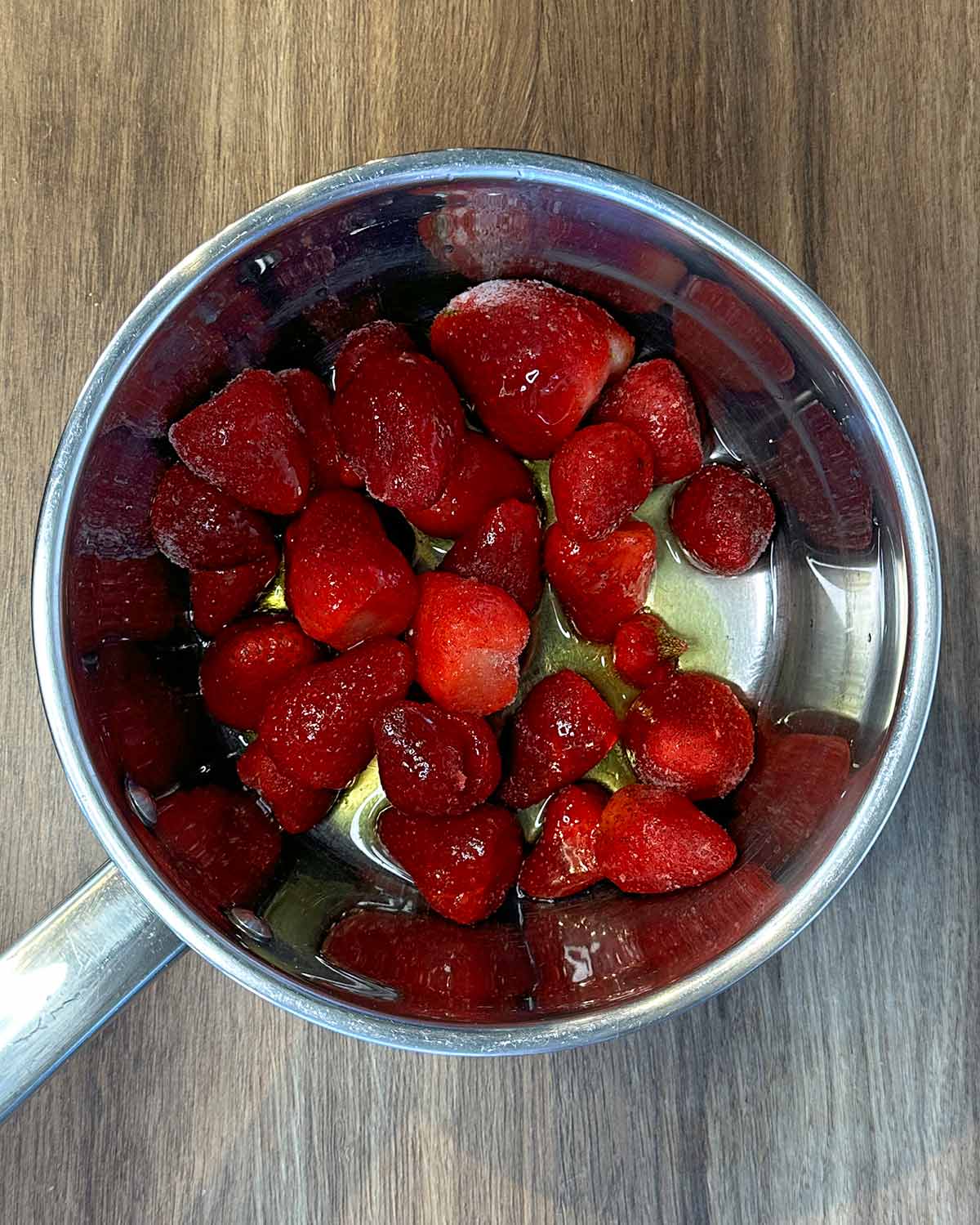 Frozen strawberries and maple syrup in a stainless steel saucepan.