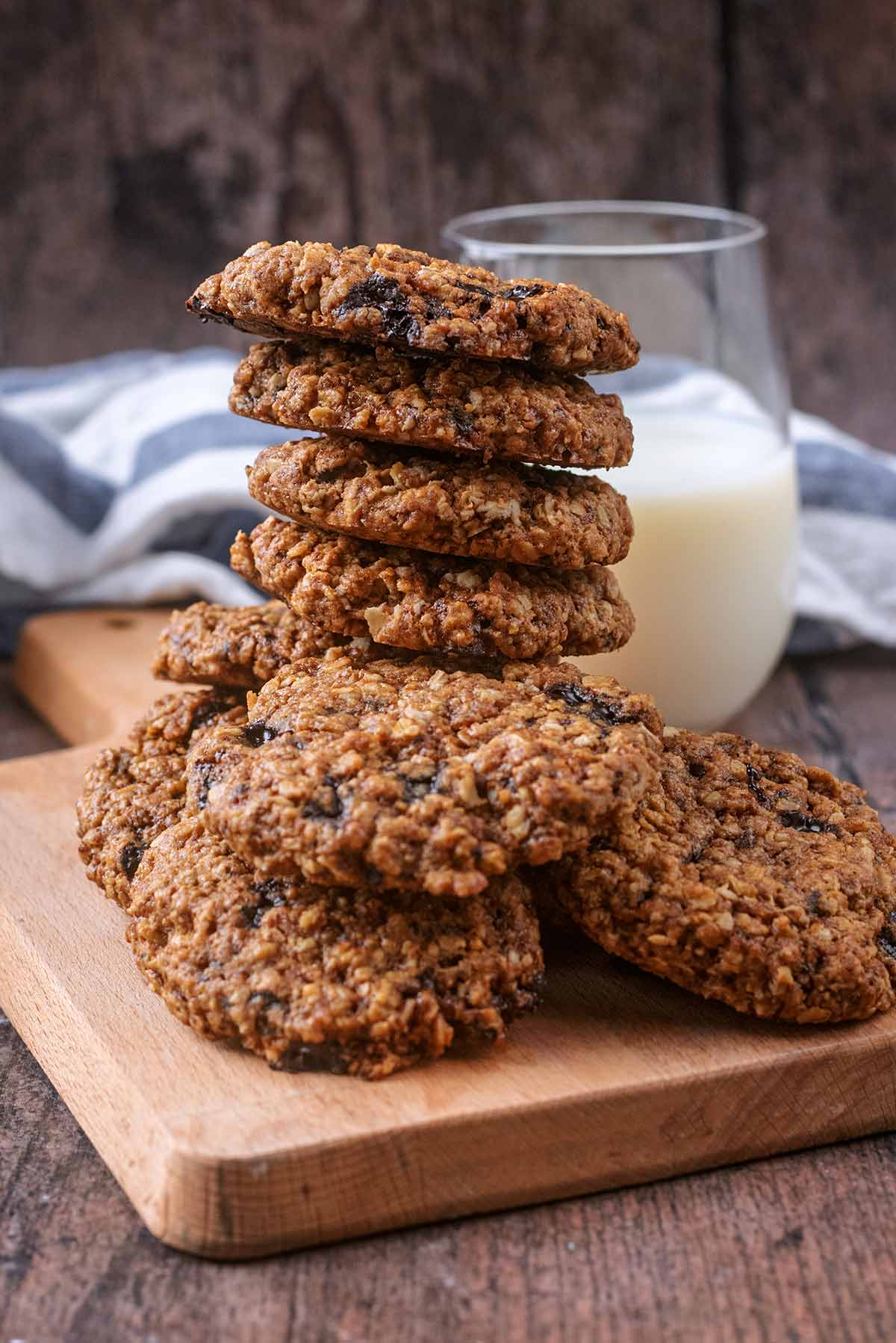 A stack of oat cookies on a wooden board with a glass of milk.
